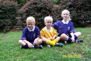 Photo of 3 blonde haired children ages 3, 5, and 7 are smiling and wearing soccer team uniforms