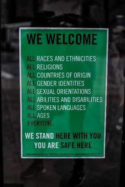 Green sign with White text stating We Welcome All